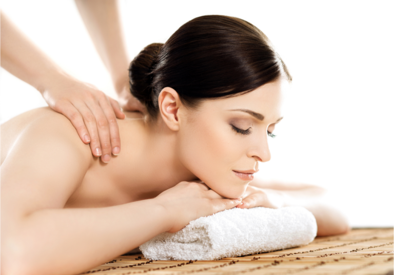 A woman with her eyes closed is lying face down on a massage table, with her head resting on a towel, while a pair of hands provides a back massage.