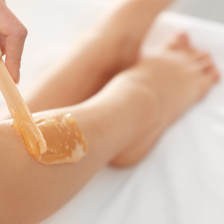 A person at Peachy Peel beauty salon in London applies honey-colored wax on their leg for hair removal on a pristine white surface.